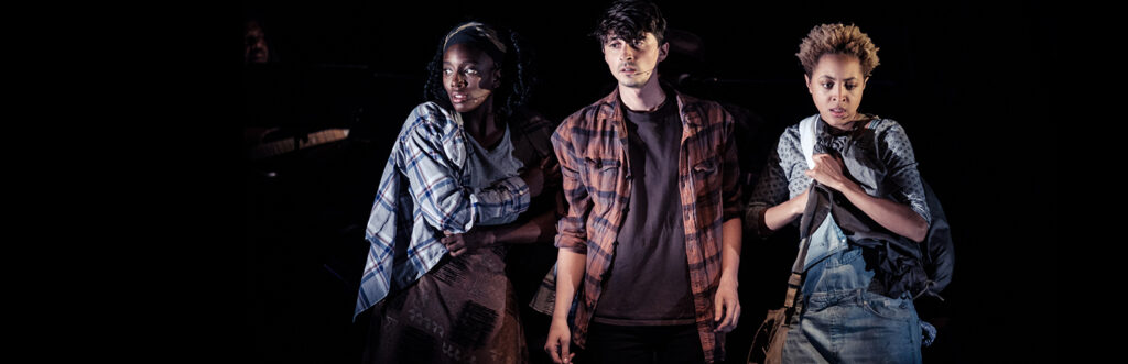 A still from Parable of the Sower featuring three characters, dressed in flannels, in the midst of the action of the plot.