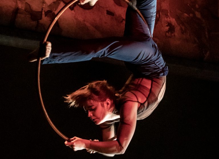 The 7 Fingers performer hanging from a hula hoop in mid air