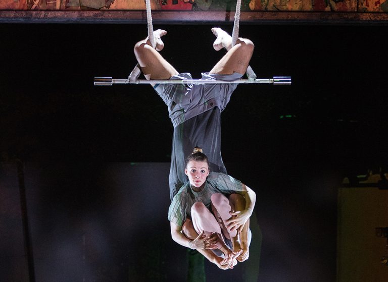 The 7 Fingers performers hanging from a bar on the ceiling