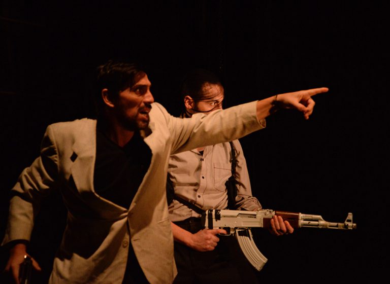 Two men pointing with guns performing in Plata Quemada
