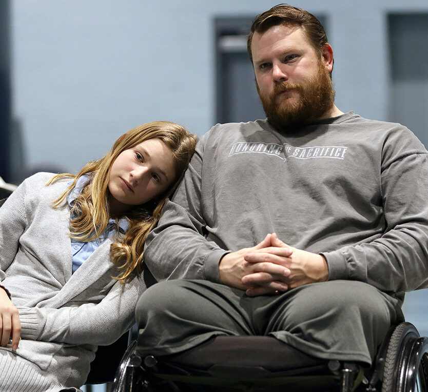 Two people in wheelchairs, one resting their head on the other