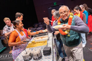 Audience members holding his bowl of dahl to the camera