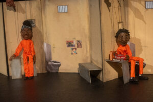 Puppets in orange in a prison cell