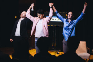 All three actors holding hands raised together