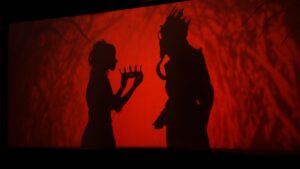 Shadow puppet giving a crown to another shadow puppet. Red background.
