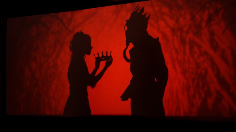 Shadow puppet giving a crown to another shadow puppet. Red background.