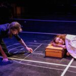 Woman writing on ground while a child sleeps and uses a suitcase as her pillow