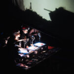 Company members producing shadow puppetry in front of a screen