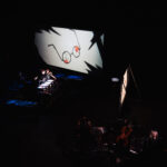 Image of glasses on a screen, people in the foreground producing shadow puppetry